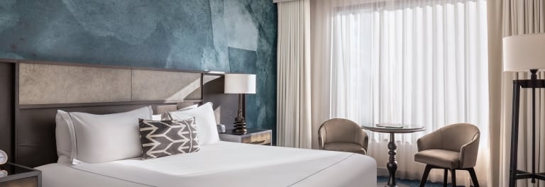 A hotel room with a king-sized bed, two armchairs, and a large window