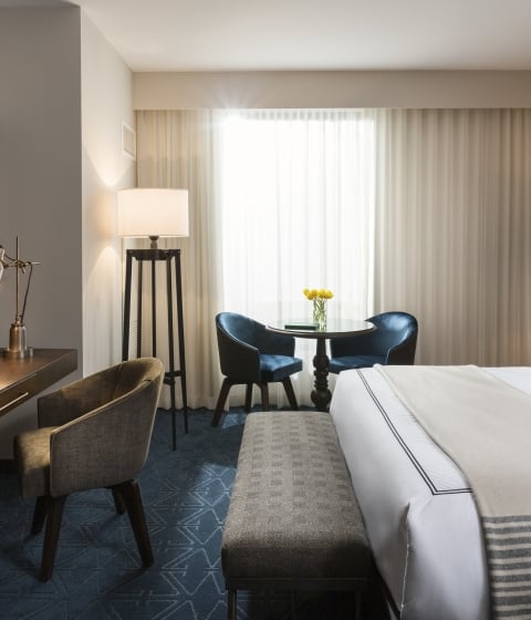 A wide view of a hotel room with a bed, table, chairs, and lamp.