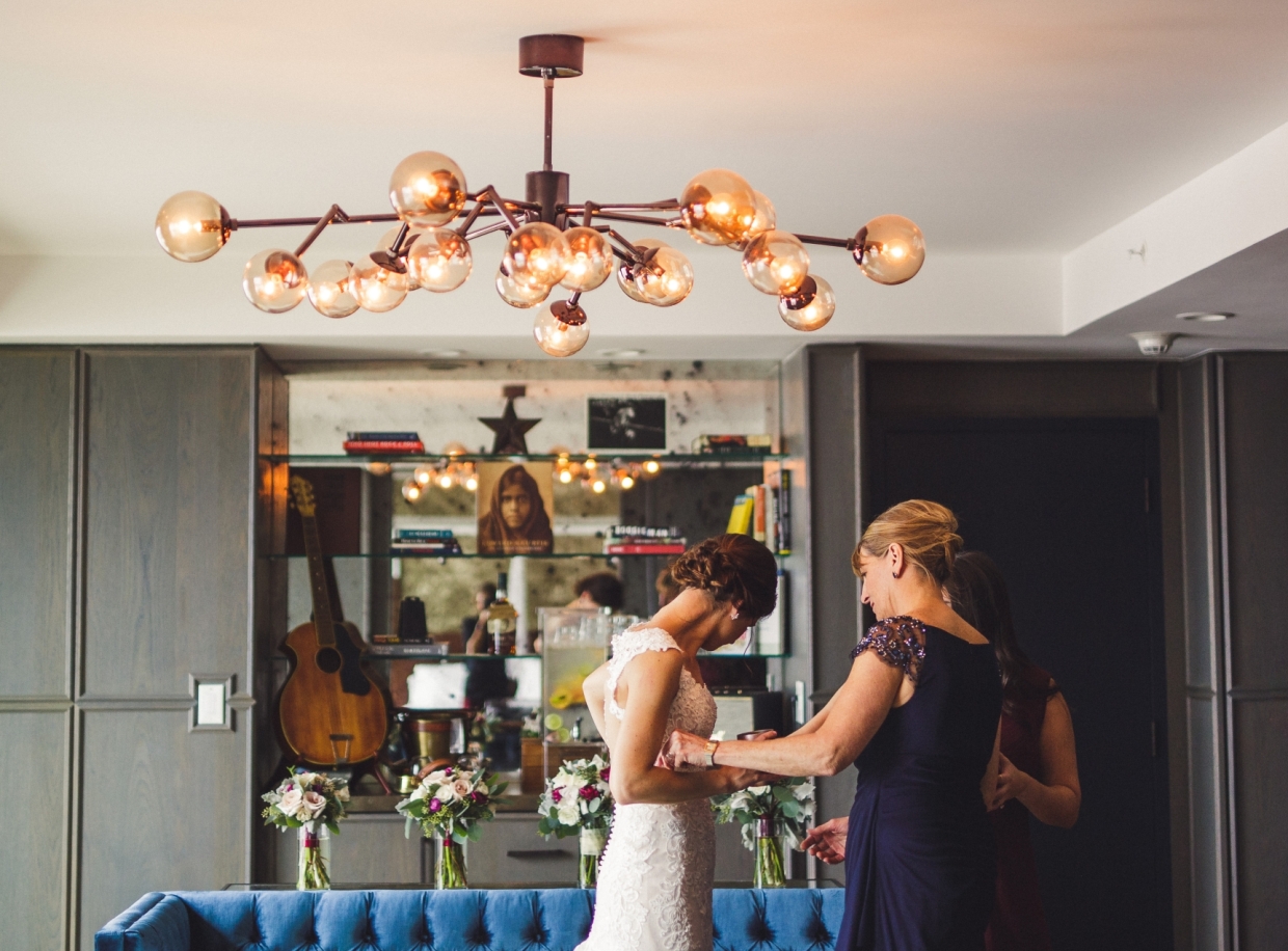 A lobby area with a chandelier, blue sofa, flowers, shelves with a guitar, and people