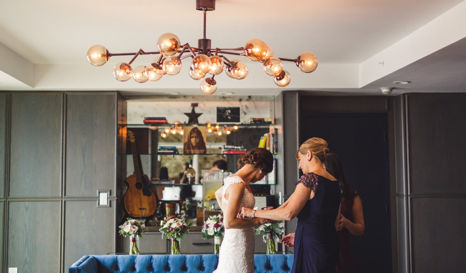A luxurious lobby with a chandelier, blue couch, flowers, and a bar in the background.