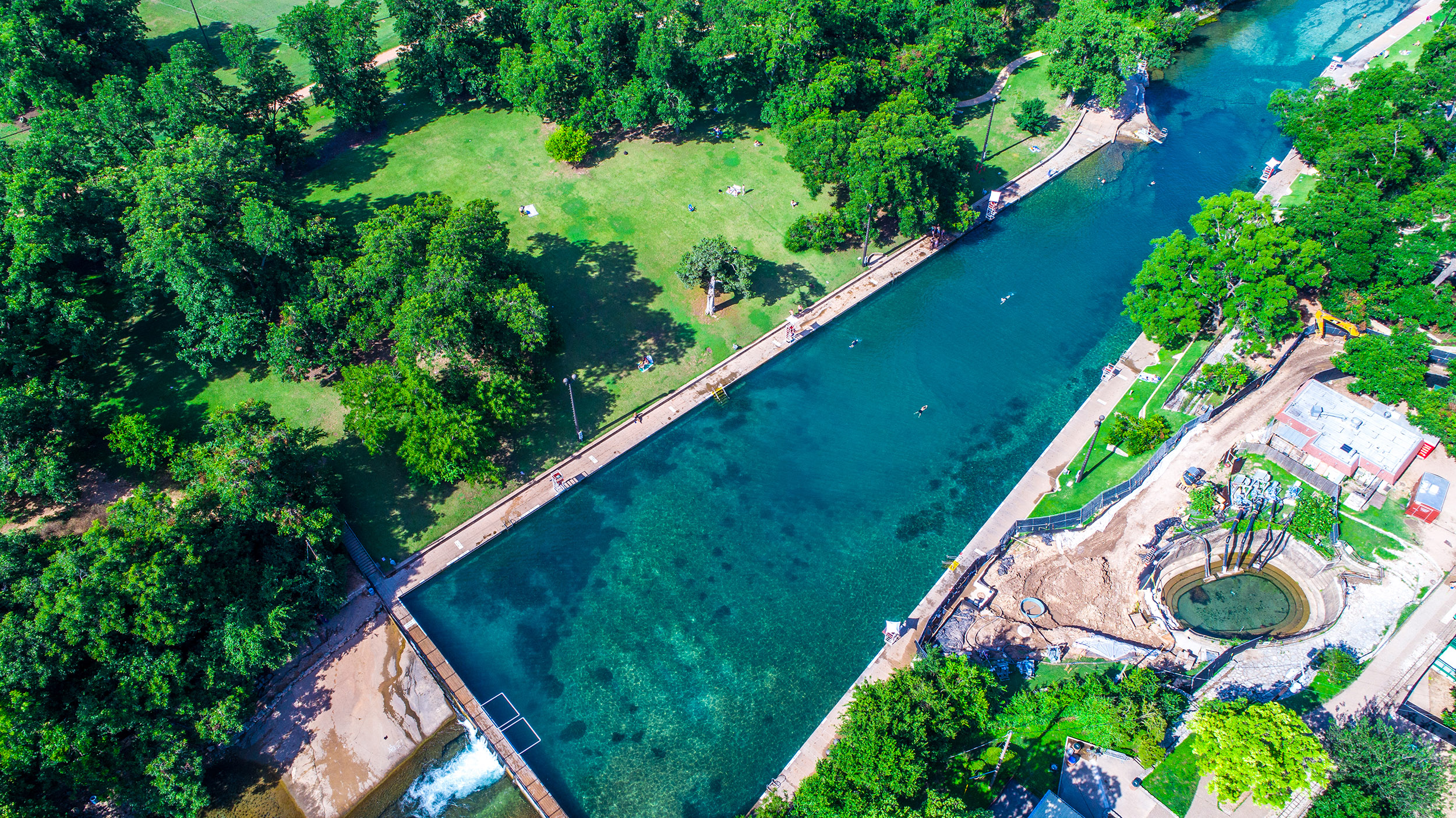 An aerial view of a large pool surrounded by trees and grass.