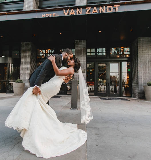 Groom holding wife and kissing her outside Hotel Van Zandt
