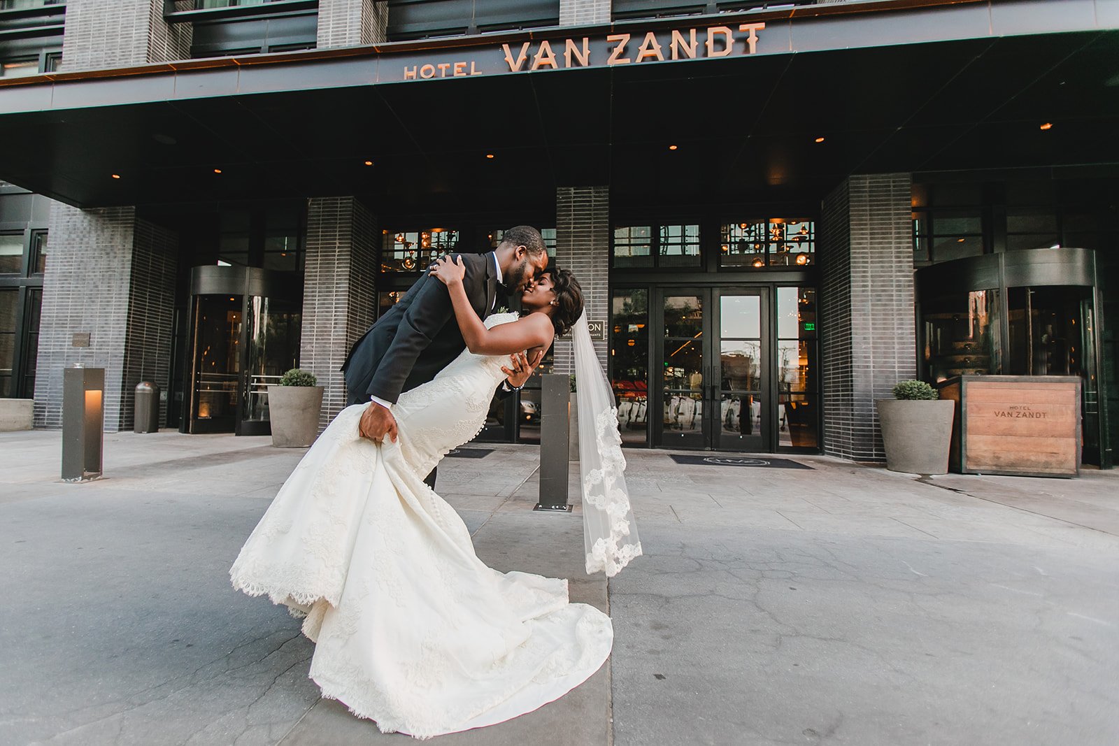 Groom holding wife and kissing her outside Hotel Van Zandt