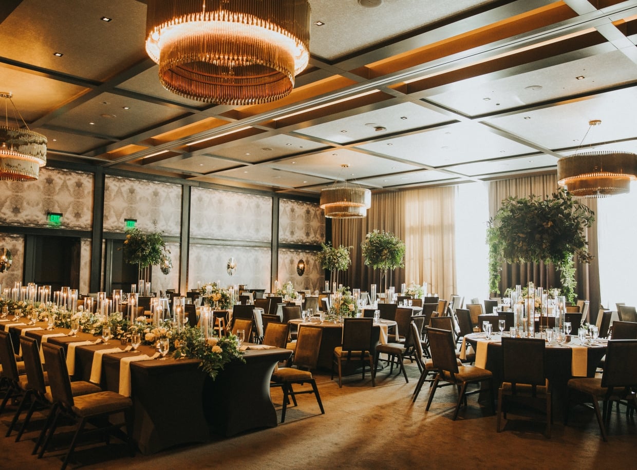 A large, elegantly set dining room with round tables, chairs, and greenery.