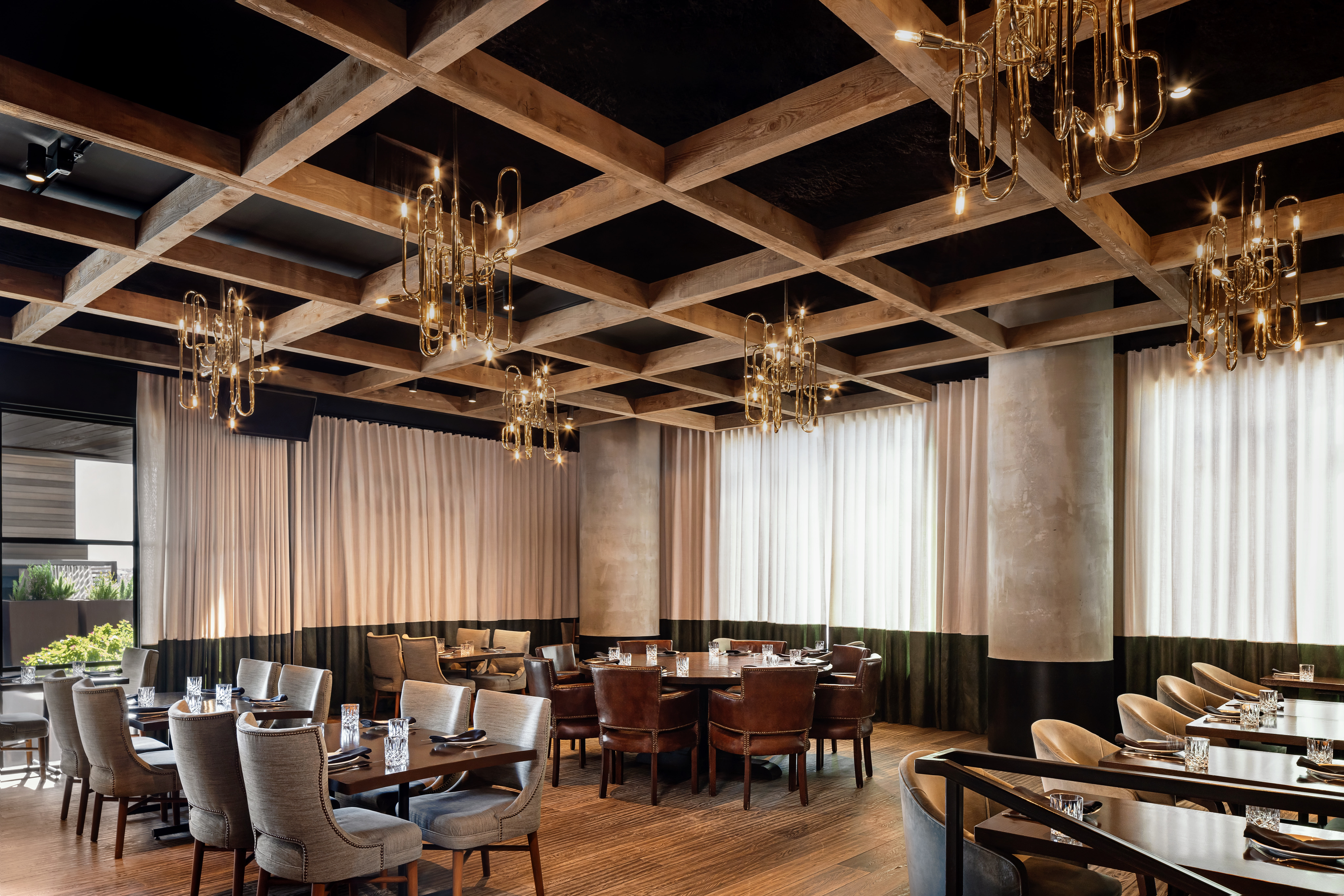 A dining area with wooden tables and leather chairs under a ceiling with wooden beams and chandeliers.