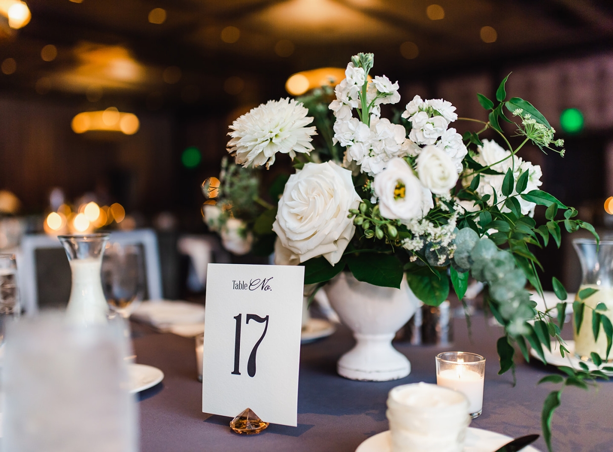 A dining table set with a floral centerpiece, table number, and candles.