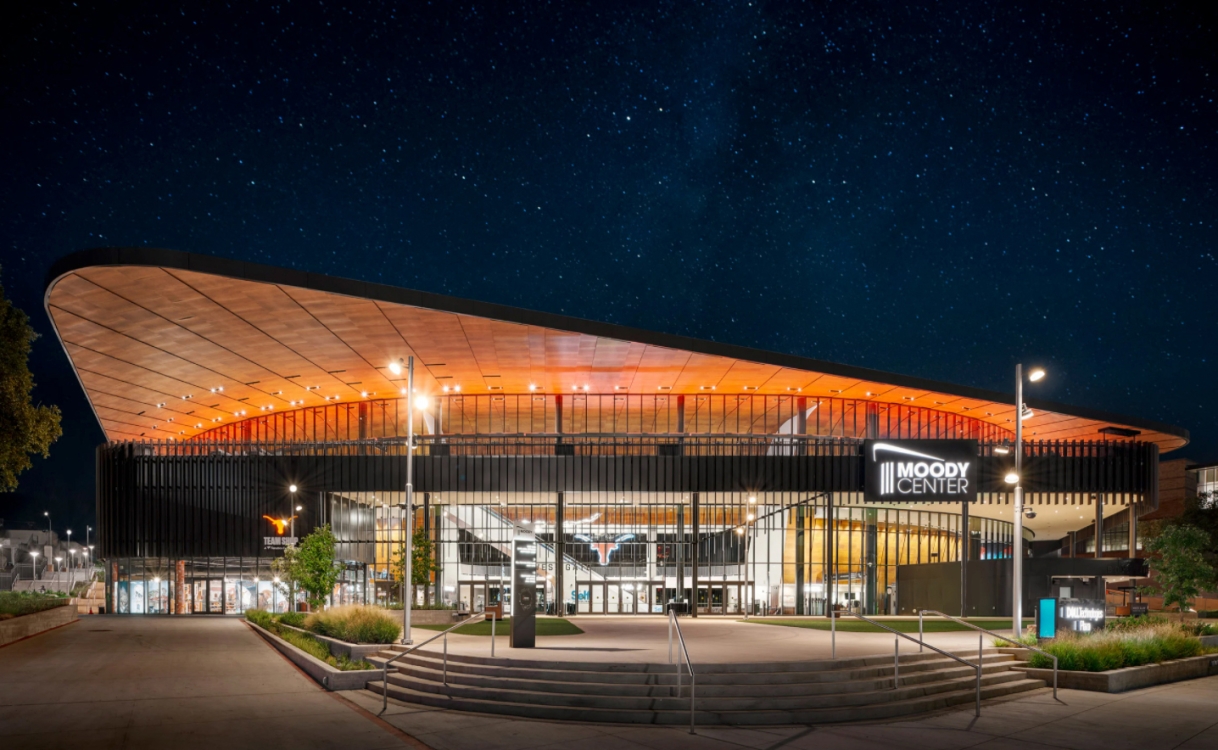 A modern building with a large curved roof and a sign reading 'Moody Center' at night.