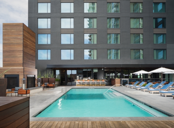A rectangular pool with lounge chairs and umbrellas in front of a large building.