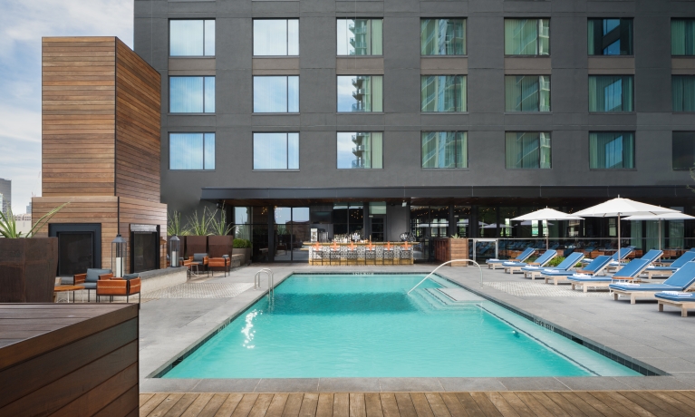 A rectangular pool with blue lounge chairs and white umbrellas in front of a gray building.