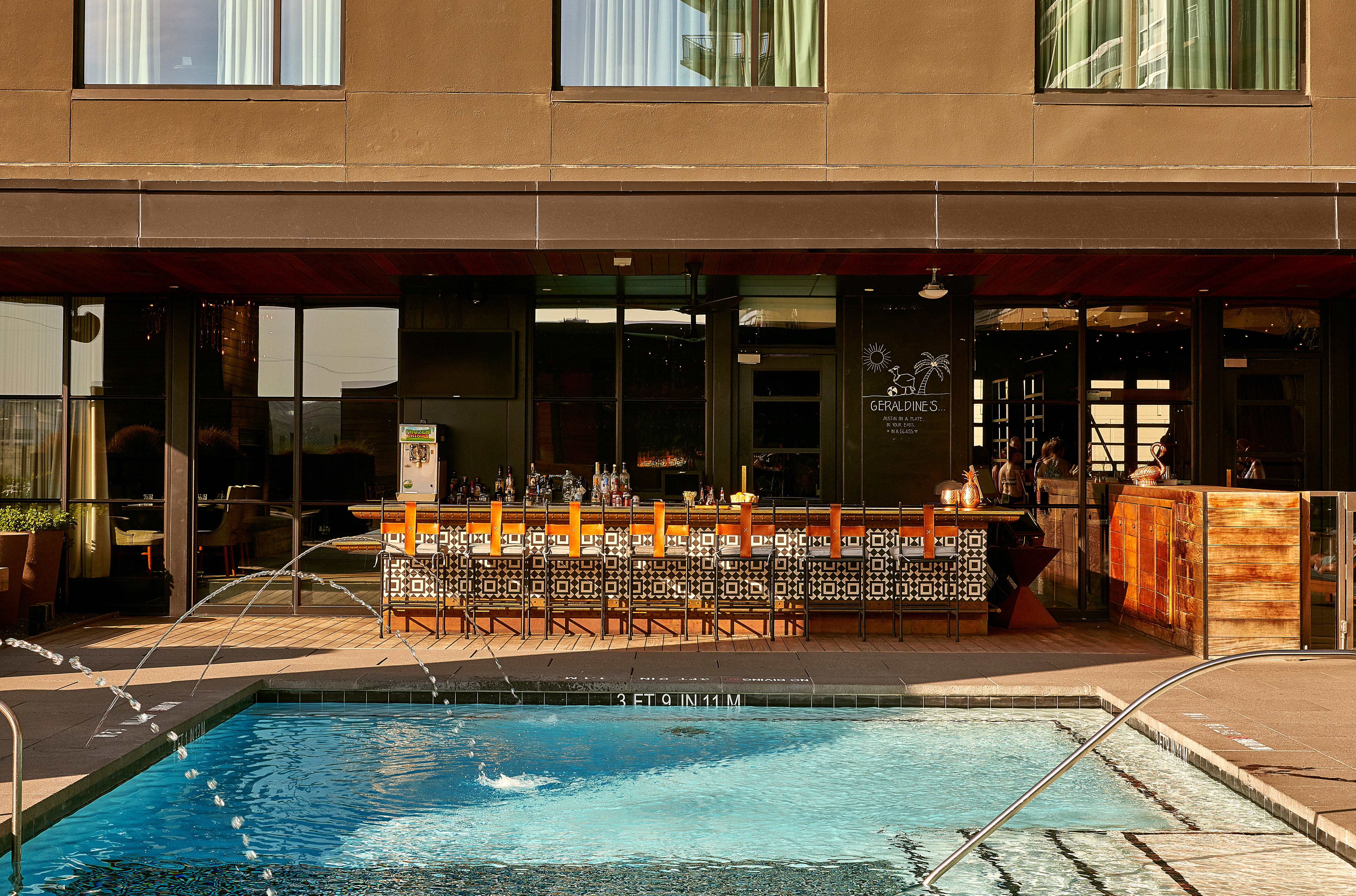 A pool with a fountain in front of a bar and building