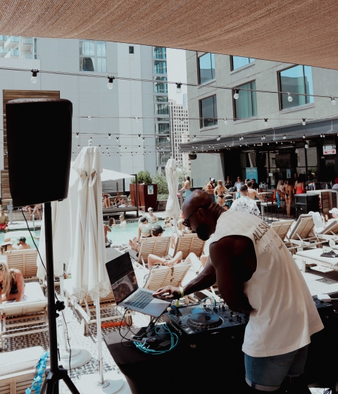 A DJ spins music at a poolside party with lounge chairs and umbrellas.