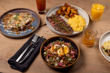 An overhead shot of a rustic wooden table set for brunch with plates of savory food, side dishes, and drinks.