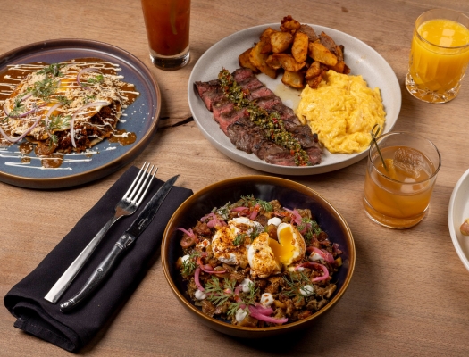 An overhead shot of a rustic wooden table set for brunch with plates of savory food, side dishes, and drinks.