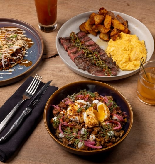 An overhead shot of a rustic wooden table set for brunch with plates of savory food, side dishes, and drinks.