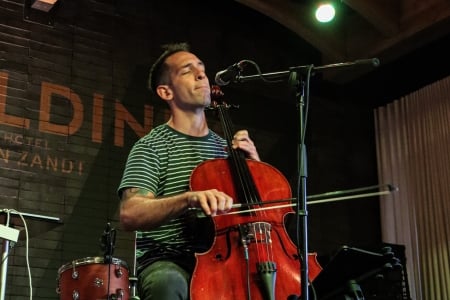 A musician playing the cello on stage under warm spotlights during a live performance.