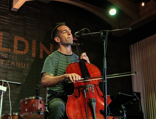 A musician playing the cello on stage under warm spotlights during a live performance.