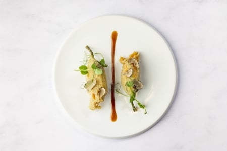 Two intricately prepared small appetizers, possibly dumplings or spring rolls, elegantly plated with a caramel-colored sauce drizzle.