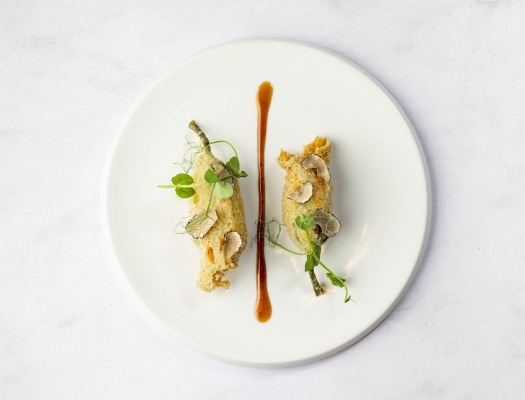 Two intricately prepared small appetizers, possibly dumplings or spring rolls, elegantly plated with a caramel-colored sauce drizzle.