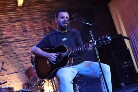 A guitarist performing on a dimly lit stage, bathed in cool blue and purple light.