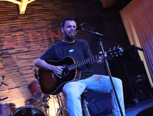 A guitarist performing on a dimly lit stage, bathed in cool blue and purple light.