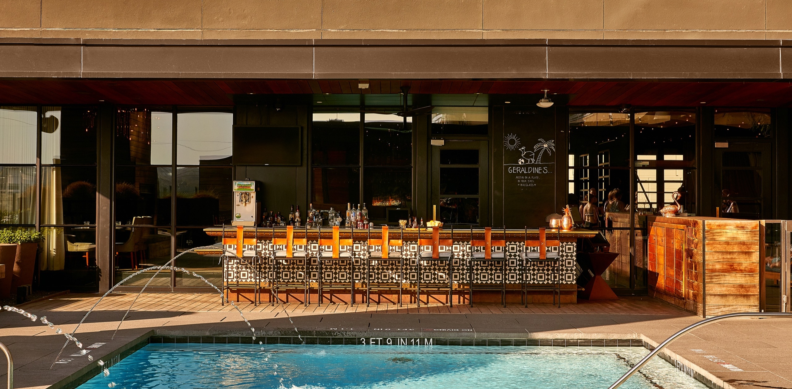 Sun-lit swim-up bar with orange stools and mosaic tile at Hotel Van Zandt's rooftop pool deck, Austin