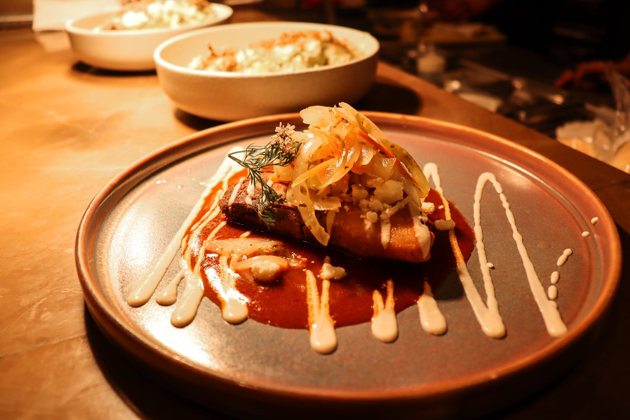 Lamb tetela on brick-red birria sauce, topped with pickled onions and crumbled queso fresco