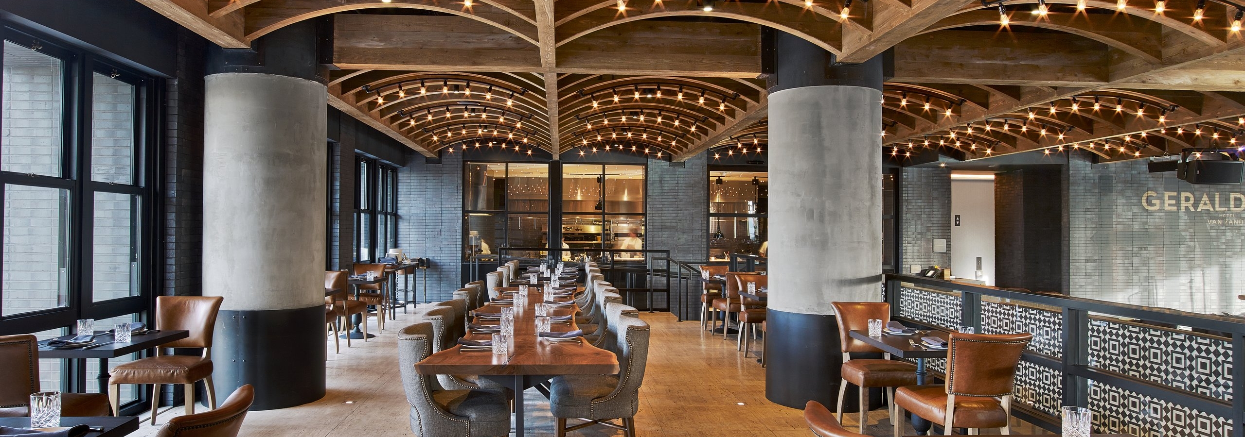 Luxury restaurant interior with curved wooden vaulted ceiling, Edison bulb lighting, leather chairs, and dark wood dining tables.