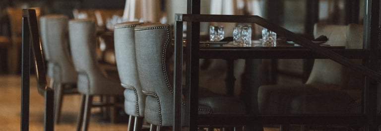 Dimly lit luxury restaurant with tall upholstered wingback chairs, crystal glasses, string lights, and illuminated stair steps.